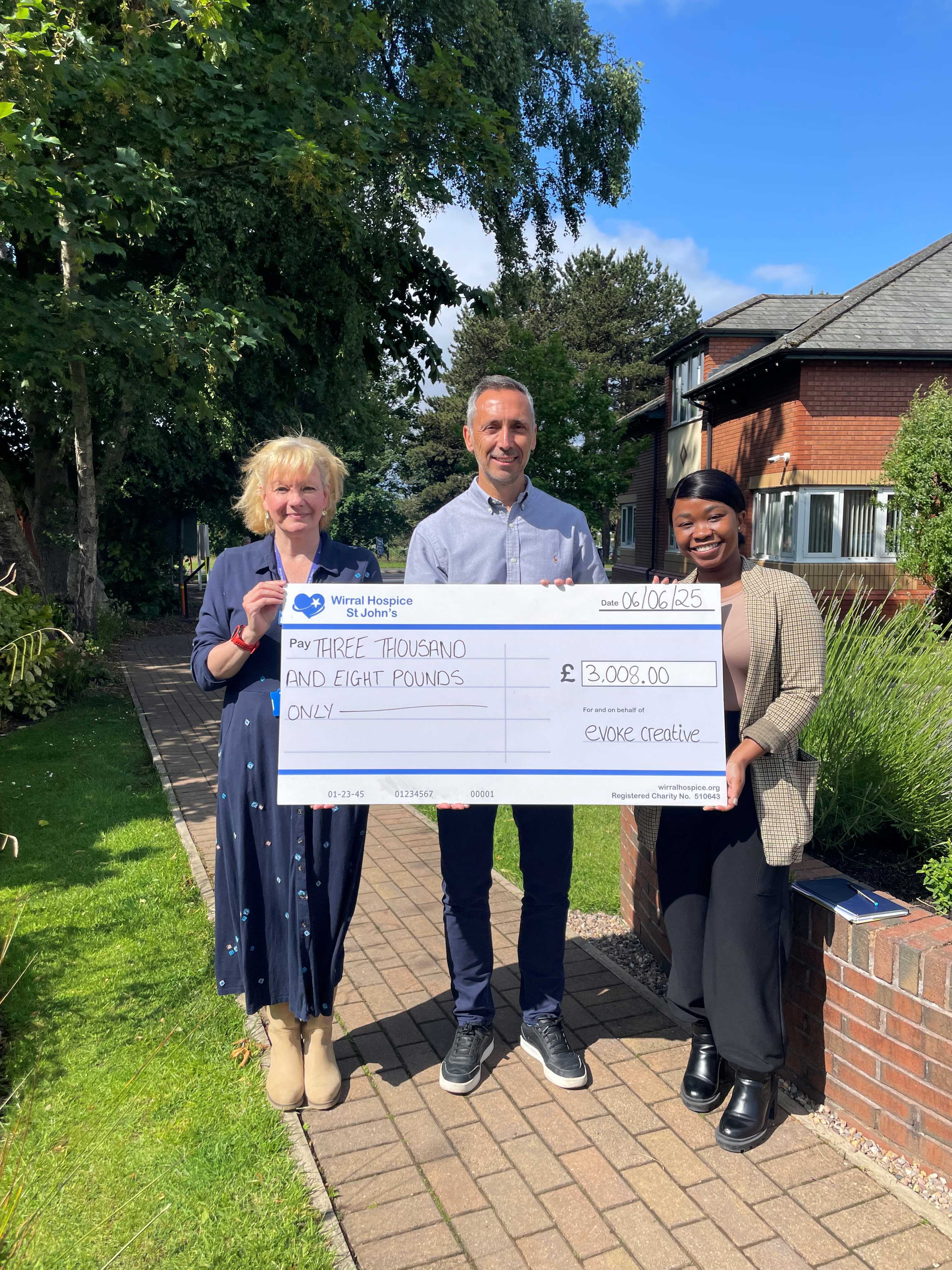 Two people from Evoke and one person from Wirral Hospice St John with a large cheque for the sum of three thousand and eight pounds